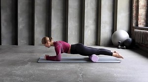 A young woman in sportswear performs a myofascial thigh massage with a roller.