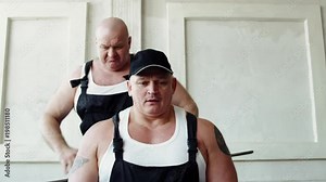 Two healthy fellow are curving a metal girder. One man is holding it and flexing around neck of second strongman, humorous show