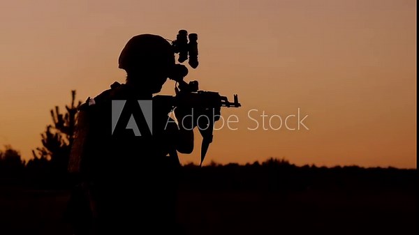 Silhouette of an armed soldier with a rifle and night vision gear against a sunset sky. Military training and tactical operation