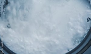 A close-up view of a washing machine filled with large amounts of white foam, illustrating the cleaning process in action