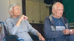 An elderly couple seated at home talking about life and experiences