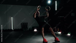 Full body shot - Sportsman using gymnastic rings to do reverse push ups in a dark moody modern gym