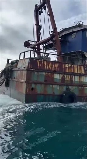 An old fishing trawler dumps nets and debris into the open ocean. Real