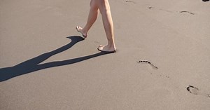 Woman Feet Walking Barefoot on Beach Leaving Footprints in Sand.