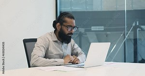 In the vibrant atmosphere of the office, an Indian office worker breaks into a genuine smile during a video call. His eyes light up as he shares positive news or experiences.