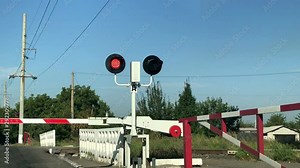Close-up of red flashing traffic lights at a railway crossing with a lowered barrier. Railroad crossing with barriers lowered and red lights flashing warning and announcing coming train on sunny day.