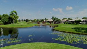 Drone flyover from the grass over water in a golf course field with trees and greenery around