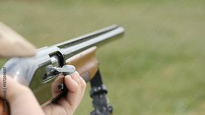 Aiming and shooting smoothbore hunting rifle and a cartridge flying away from a breechblock in a field in slow motion. The rifle looks modern and effective in a sunny day in autumn.