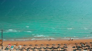 People walk on beach of Adriatic sea with turquoise water and light rolling waves. Sandy beach equipped with sunshades and deck chairs aerial view