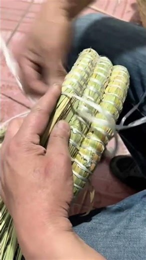 weaving dried straw bundles together using thin white strings to create traditional handicraft