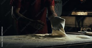 Super slow motion macro of artisan baker is making pizza dough with flour dust scattering during making homemade traditional recipe italian pizza in traditional bakery or pizzeria restaurant kitchen.