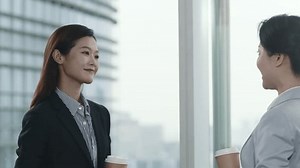two asian business women standing and chatting by the window in modern office