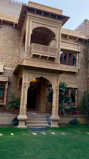 traditional Rajasthani Haveli made of golden Jaisalmer stone, showcasing intricate stone latticework (jalis), elaborately carved balconies (jharokhas), arched doorways, and domed chhatris on the rooftop. The façade should reflect authentic 18th-century Marwari architecture, with symmetrical layout, detailed motifs, and sandstone carvings of flora, fauna, and geometric patterns. #housedesign #elevation #design #gulaaldesignstudio2 #architectdigestindia #jaisalmer | Gulaal Design Studio