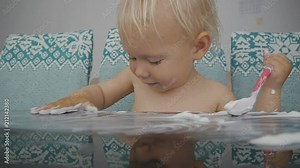Baby eating yogurt making a mess. Close-up shot of cute baby girl smearing yogurt on the black glass table with spoon and palm