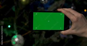 Christmas background. Chromakey. Mobile phone with blank green screen in landscape format on xmas tree