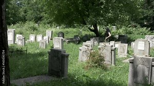 Young woman dressed in funeral clothes walking in cemetery among the graves