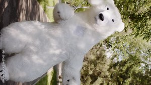 Vertical view of a giant polar bear puppet doll jumps and dances with balloons in a green park, in a background of green trees, in summer, outdoors. The concept of recreation, children's party