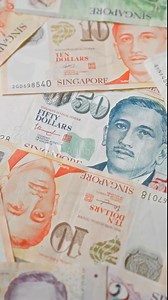 Singapore dollar banknotes scattered in a close-up shot, showcasing various denominations including ten and fifty dollars, with clear details of the country's currency.