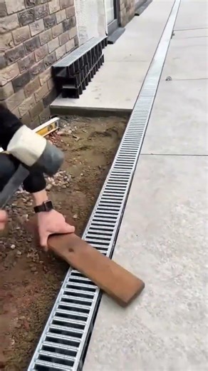 installing a long metal drain into a fresh cement base with a mallet on a construction site outdoors