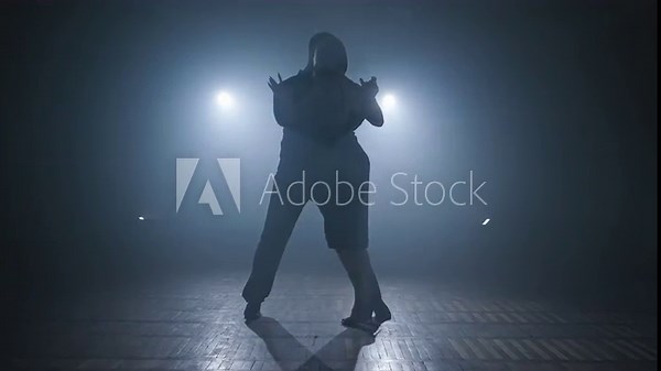 Young couple dance tango in dark room with smoke and spotlights in slow motion. Silhouette of dancers in smoky ballroom. Wide angle in 4K, UHD