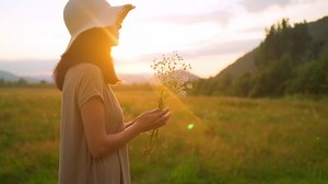 side view cheerful woman in straw hat posing with wildflowers in the sun rays standing on the meadow at sunset slow motion countryside landscape