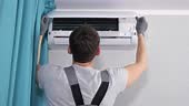 Man worker in gray t-shirt opens broken white air conditioner unit...