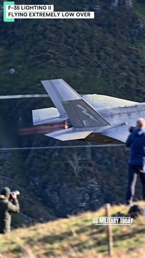 an F-35 fighter jet flying extremely low over a grassy hillside