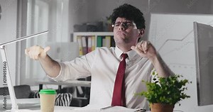 Successful accountant dancing sitting on chair celebrating a strike of profitable deal. Portrait of happy bank employee signing beneficial contract