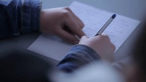 In Elementary School Class Student writes in notebook. education, elementary school, learning and people concept - group of school kids with pens and notebooks writing test in classroom