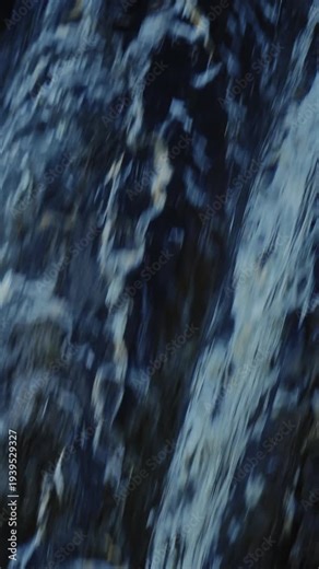 Abstract close up of vertical waterfall with motion blur as water rushes over dark rock, creating a dynamic natural texture.