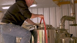 Male brewer cleaning a fermentation tank at a craft brewery with a hose