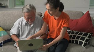 Daughter teaching her father computer skills in living room. Asian man with white beard and young woman sitting in living room using laptop. Senior lifestyle family concept.