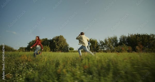 Three young friends are having fun and running around the field on a sunny summer day. Holidays in the countryside