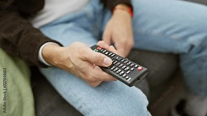 A man comfortably holds a remote control while relaxing on a couch in a home setting, ready to watch television.