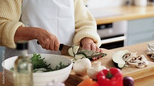 healthy eating, food cooking and culinary concept - hands of senior woman with knife chopping zucchini on kitchen