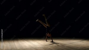 Little girl gymnast doing a somersault in the studio on a black background, slow motion.