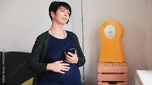 A pregnant woman using the phone app, feeling contractions before childbirth. Application with time control and tips for relaxation and breathing during pain. The yellow clock is nearby.