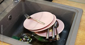 Kitchen sink filled with pile of dirty dishes and food waste pieces in strainer. Post-meal chores essential for maintaining clean home environment