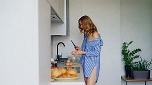 Sexy Girl in Shirt Breaking Eggs Into Glass Bowl in Kitchen. Pretty