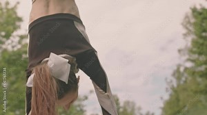 Muscular base athlete lifting up and holding flyer girl above head while practicing cheerleading stunt on sports field
