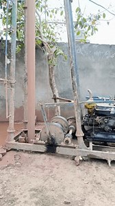 A traditional water bore drilling machine operating outdoors with muddy water flow. Old mechanical equipment used for groundwater extraction.