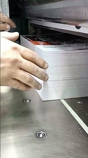 cutting a thick stack of white paper using a large industrial paper cutter machine in a workshop