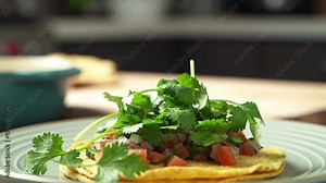 Cilantro falling onto a tortilla with fresh tomato and onion topping