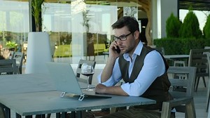 bearded businessman in formal wear talking with client by phone and smiling while sitting in office. businessman dressed in white shirt sitting in cafe and using computer while talking by his phone