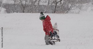 Boy tries to sledding little sister or brother but the sled is too heavy. Children have fun in winter during snowfall.