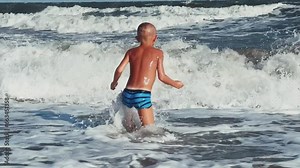 A child swims in the Sea of Azov. A boy jumps into the sea waves from the beach. The boy dives into the foaming wave. The delight of a child from a vacation at the sea. Happy moments with children. 4K