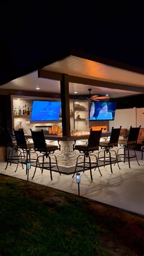 BBQ Islands & Designs on Instagram: "This is what happens when your backyard becomes the favorite place to gather 🔥✨ Designed as a complete entertainment hub, this custom outdoor kitchen brings together a fireplace, media wall, and L-shaped BBQ island under a beautifully finished patio cover. Perfect for game nights, celebrations, and relaxed evenings with family and friends. The fireplace anchors the space with a 75" TV above the mantle, while the media wall adds a full bar center, shelving, s