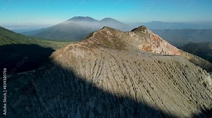 Stunning Ijen volcano mountain landscape with a crater rock mountain, lush vegetation, a valley, and a clear blue sky.