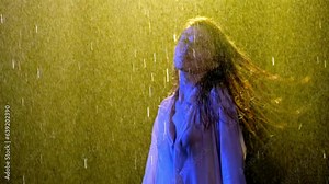 Model in wet white clothes moves and poses for video under water stream . Brunette girl scatters wet hair to different sides