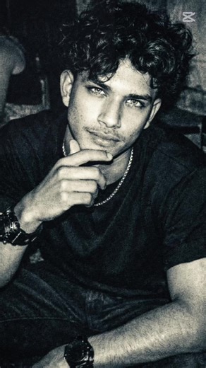 #CapCut Prompt: High-contrast black and white photo taken with a 1990s disposable camera at a dark house party. A handsome young man with dark hair and a sharp jawline is starting directly into the lens. Focus on the eyes: intense, light-coloured irises with a piercing, predatory gaze, slightly heavy-lidded (siren eyes), reflecting the harsh camera flash. He is wearing a black shirt. The image is grainy, lo-fi, with a “dark academia” bad boy